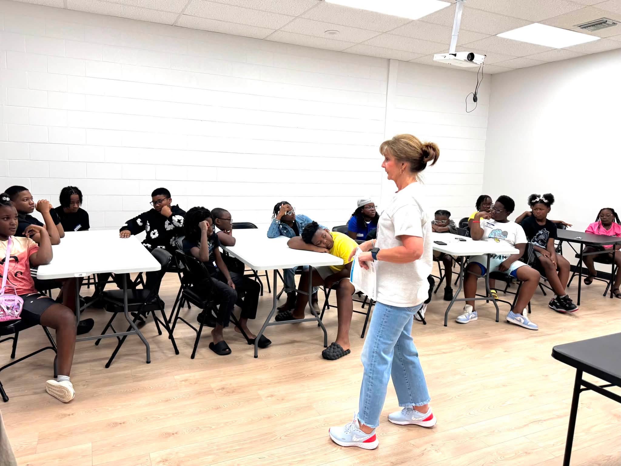 A woman talking to a group of kids in a room.